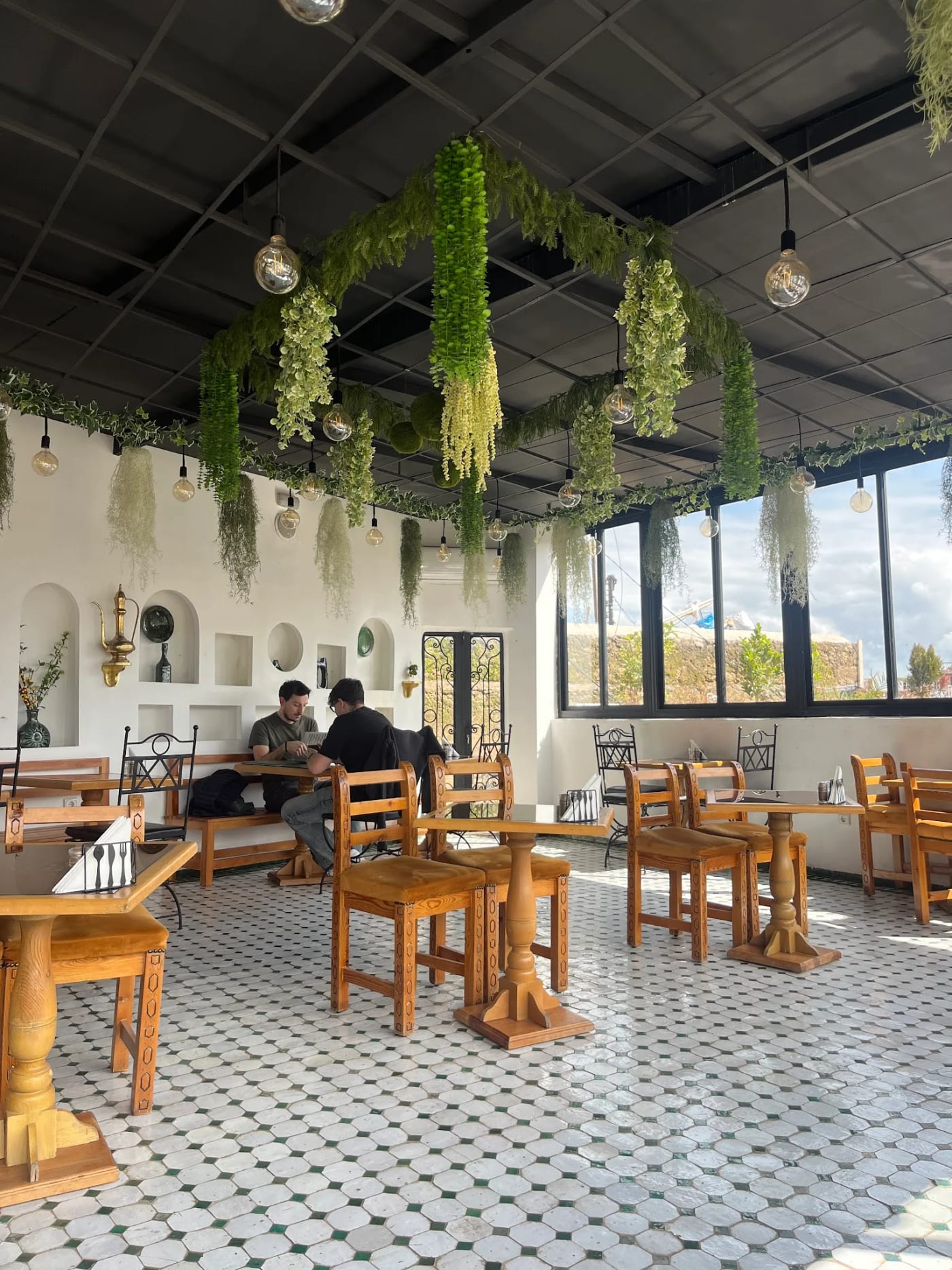 Grande salle intérieure claire avec tables en bois, banquettes et plantes suspendues